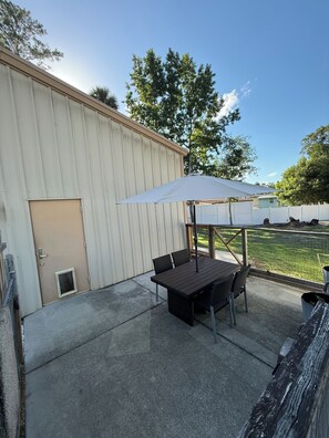 A patio area with a table and chairs, a white umbrella, and a view of a grassy yard. - 2-bedroom barndominium in peaceful Astor on a canal (Astor)