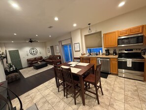 A modern kitchen with stainless steel appliances, a dining area with a wooden table and chairs, and a living room with a brown leather sofa and a ceiling fan. - 2-bedroom barndominium in peaceful Astor on a canal (Astor)