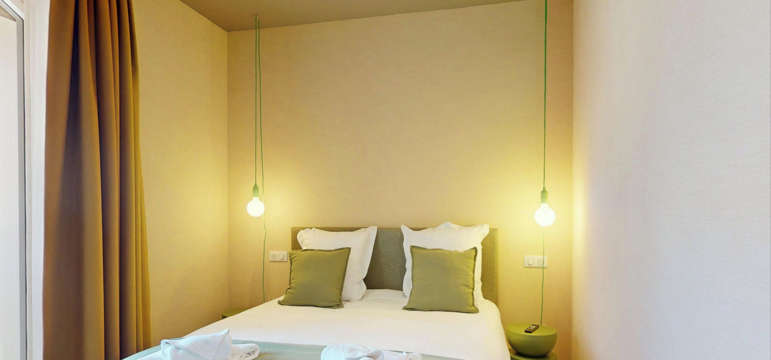 Ein Hotelzimmer mit einem Bett, zwei Nachttischlampen und einem Nachttisch mit Fernbedienung.