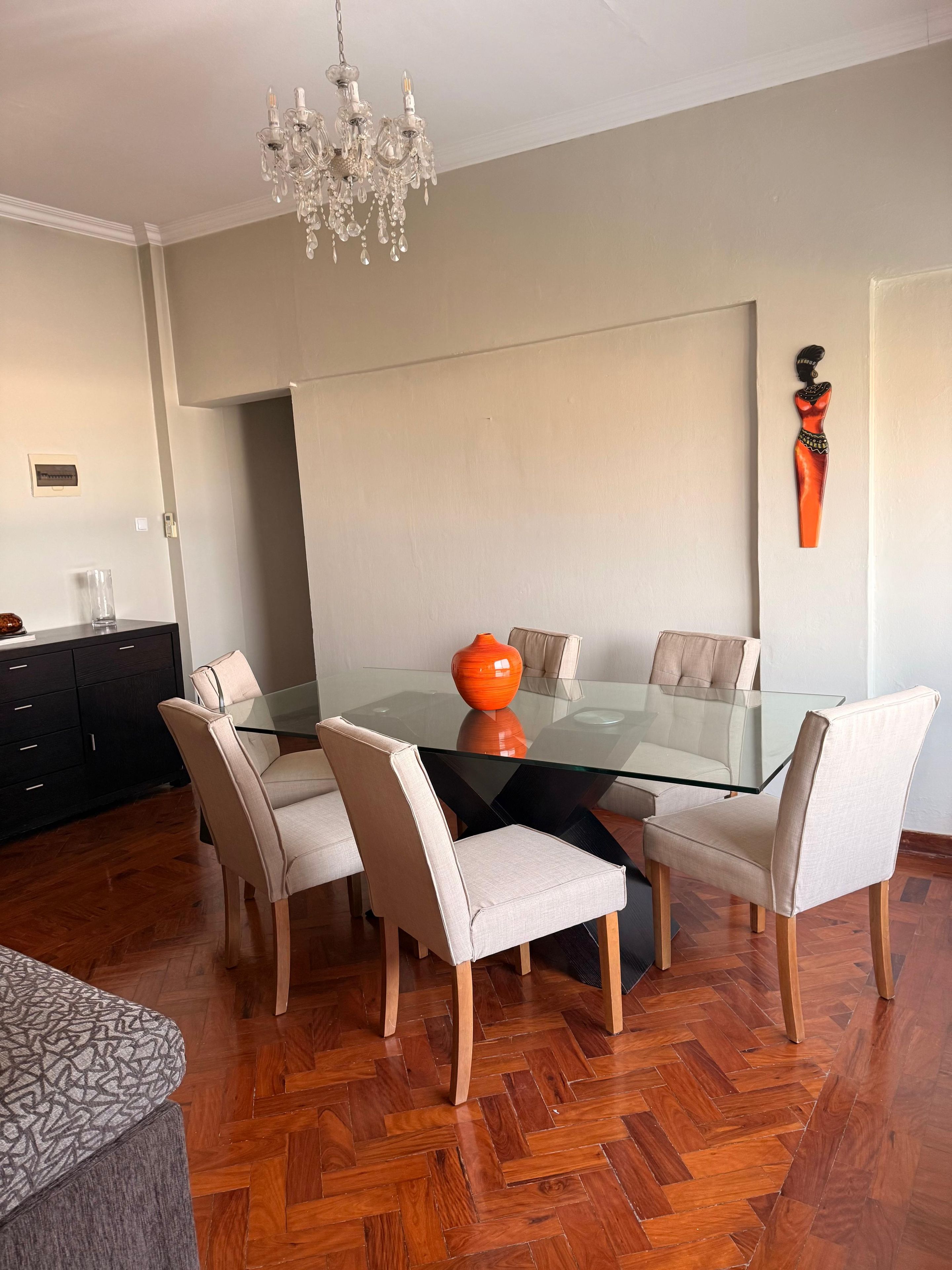 A dining area with a glass table surrounded by chairs, a chandelier, and a decorative piece on the wall.