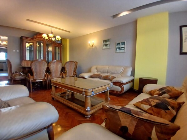 A living room with a sofa, armchairs, a coffee table, and a dining area with chairs and a table.