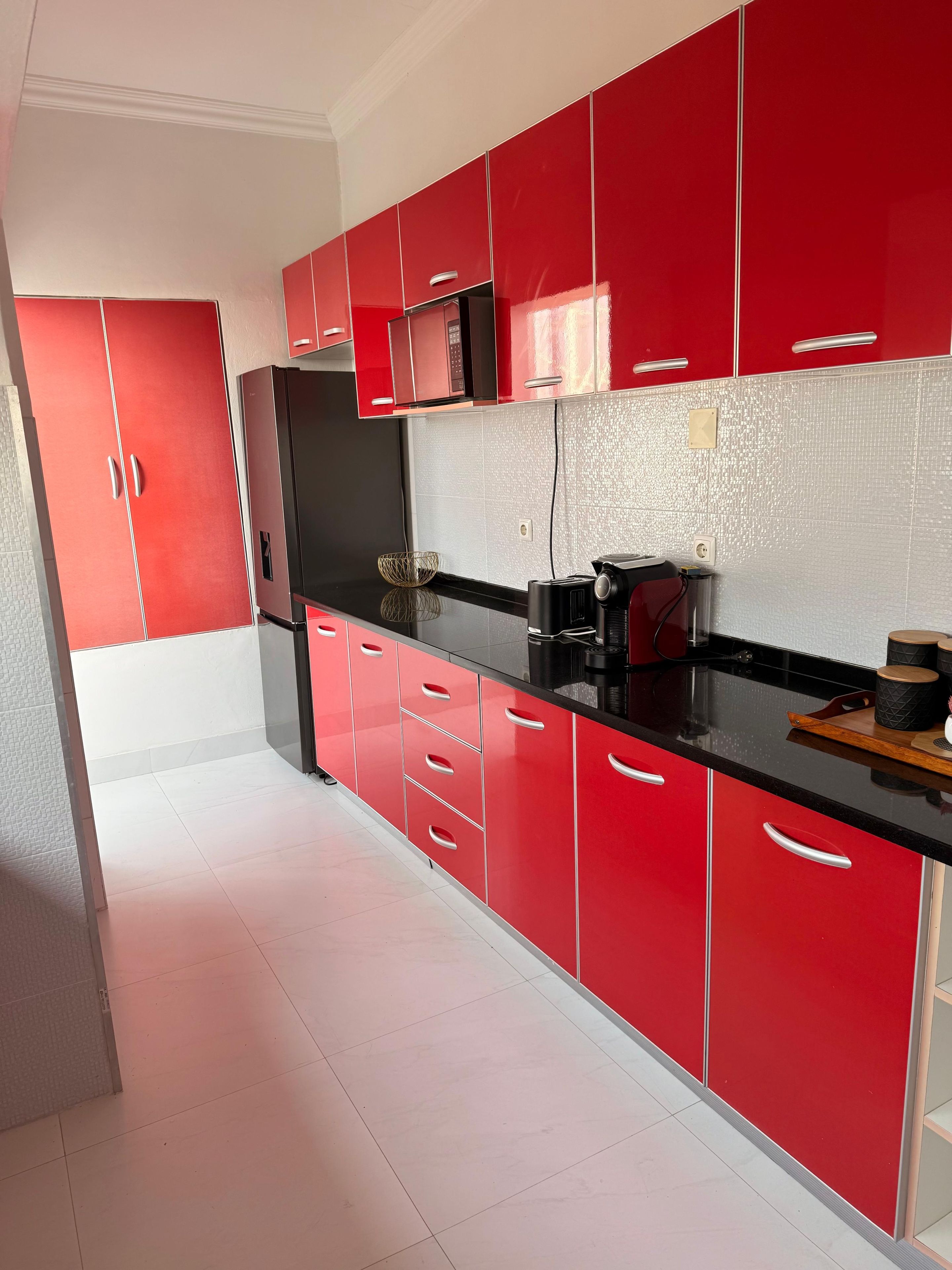 A modern kitchen with red cabinets, black countertops, and stainless steel appliances.