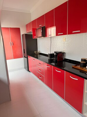 A modern kitchen with red cabinets, black countertops, and stainless steel appliances. - The Oasis Haven Beach House (Maputo)