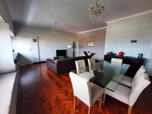 Een moderne woonkamer met een glazen eettafel, banken en een kroonluchter.