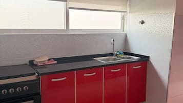 Cocina compacta con estufa a gas, armarios rojos, un lavamanos y una ventana sobre la encimera.