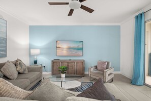 A living room with a ceiling fan, a coffee table, a sofa, a chair, a TV, and a painting of a beach scene. - 3 Themed BRs - Heated Pool, Spa & Kids Playroom (Davenport)