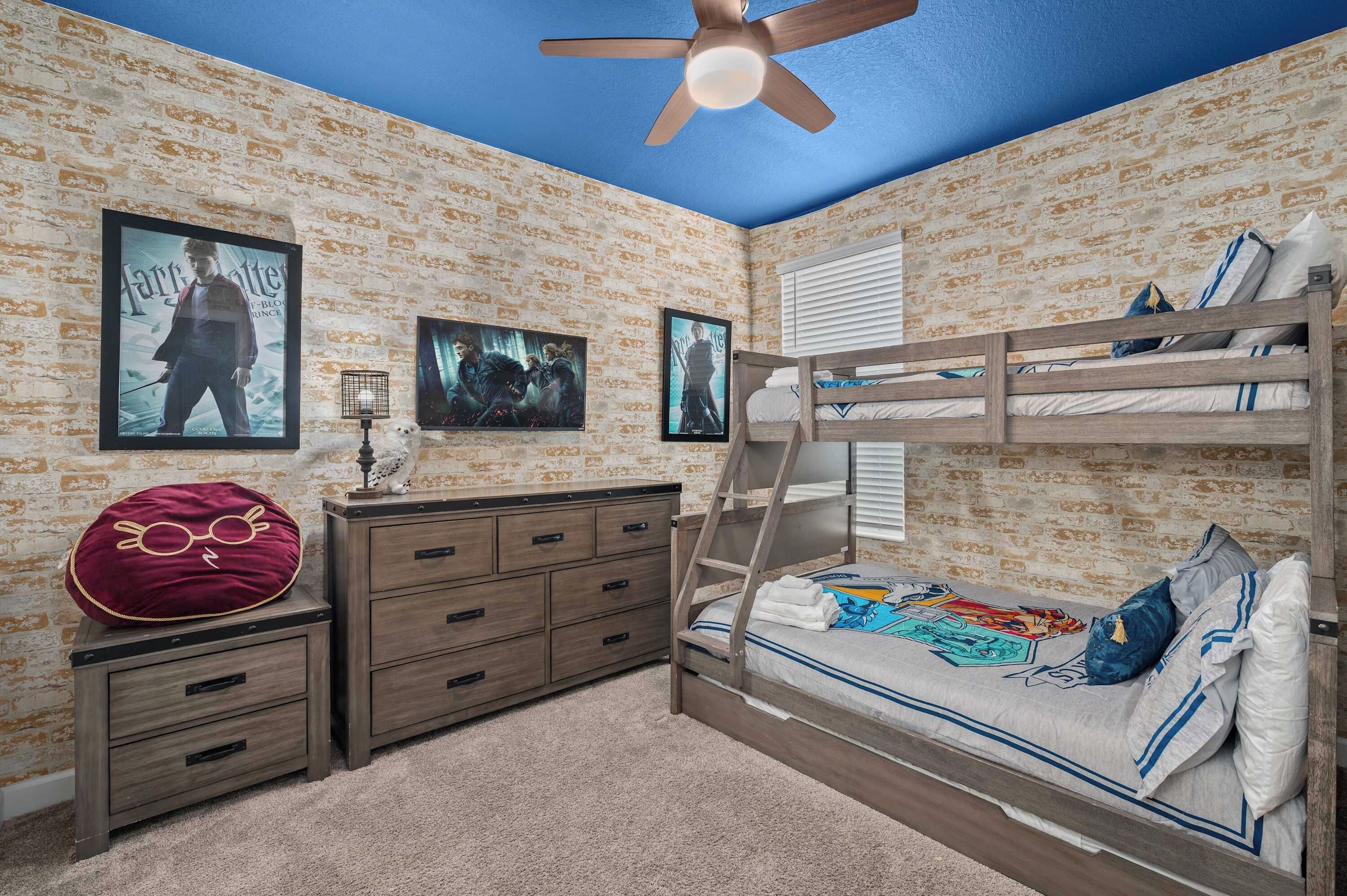 Une chambre avec un lit superposé, une commode, un ventilateur de plafond et des affiches accrochées au mur.