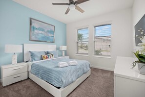 A bedroom with a bed, two bedside tables, a ceiling fan, a window with blinds, and a wall-mounted painting. - 3 Themed BRs - Heated Pool, Spa & Kids Playroom (Davenport)