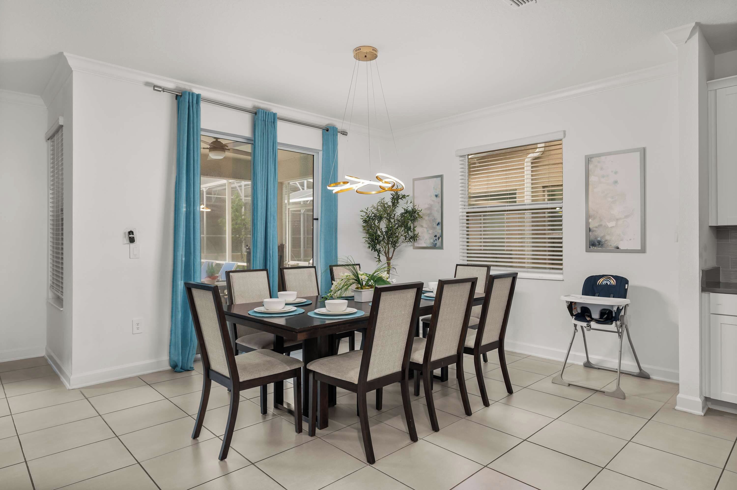 Un coin repas avec une table dressée pour six personnes, des chaises, une plante en pot et un luminaire suspendu au plafond.