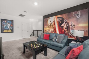 A living room with a Star Wars themed wall art, a sofa, a coffee table, and a foosball table. - 3 Themed BRs - Heated Pool, Spa & Kids Playroom (Davenport)
