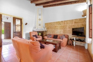 A living room with a stone wall, a television, and a fireplace. - Villa 'Roig' with Private Pool, Wi-Fi and Air Conditioning (Illes Balears)