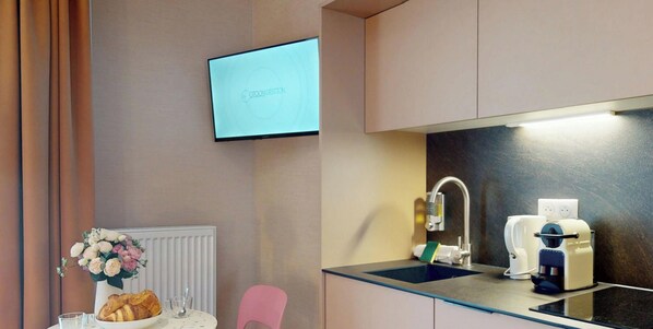 Eine moderne Küchenzeile mit Spüle, einer Kaffeemaschine und einem an der Wand befestigten Flachbildfernseher.