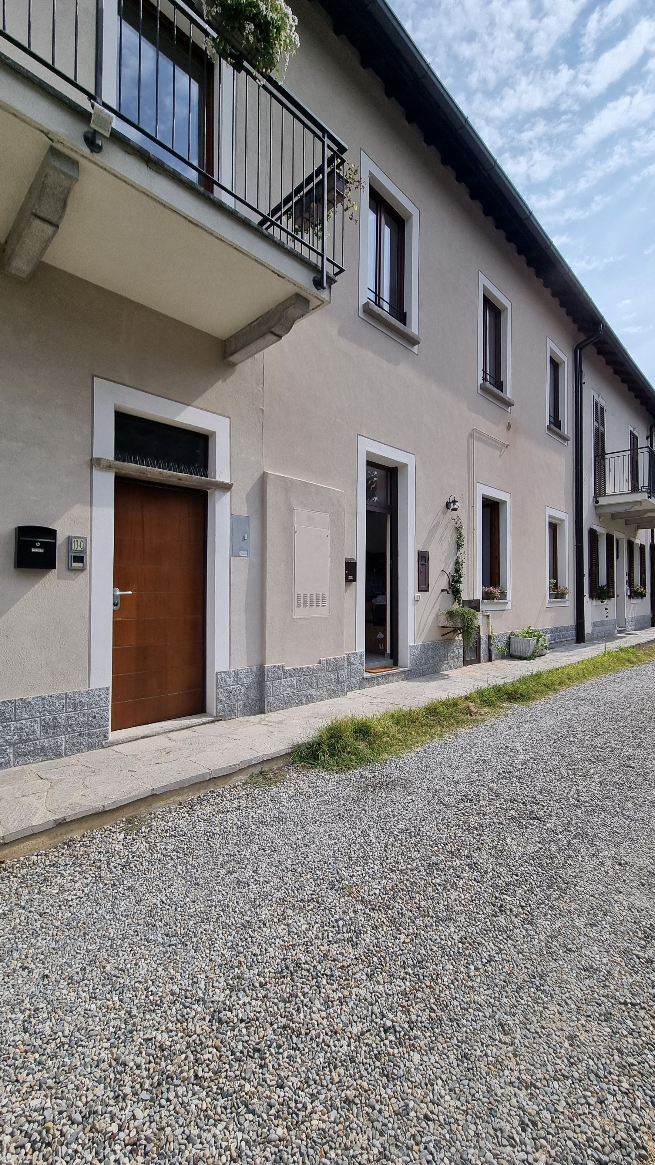 Un edificio con vialetto sterrato, porta in legno e balcone con ringhiera in metallo.
