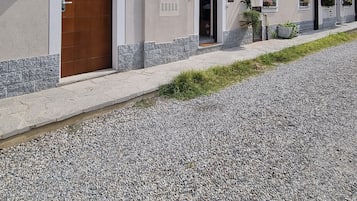 Un edificio con vialetto sterrato, porta in legno e balcone con ringhiera in metallo.