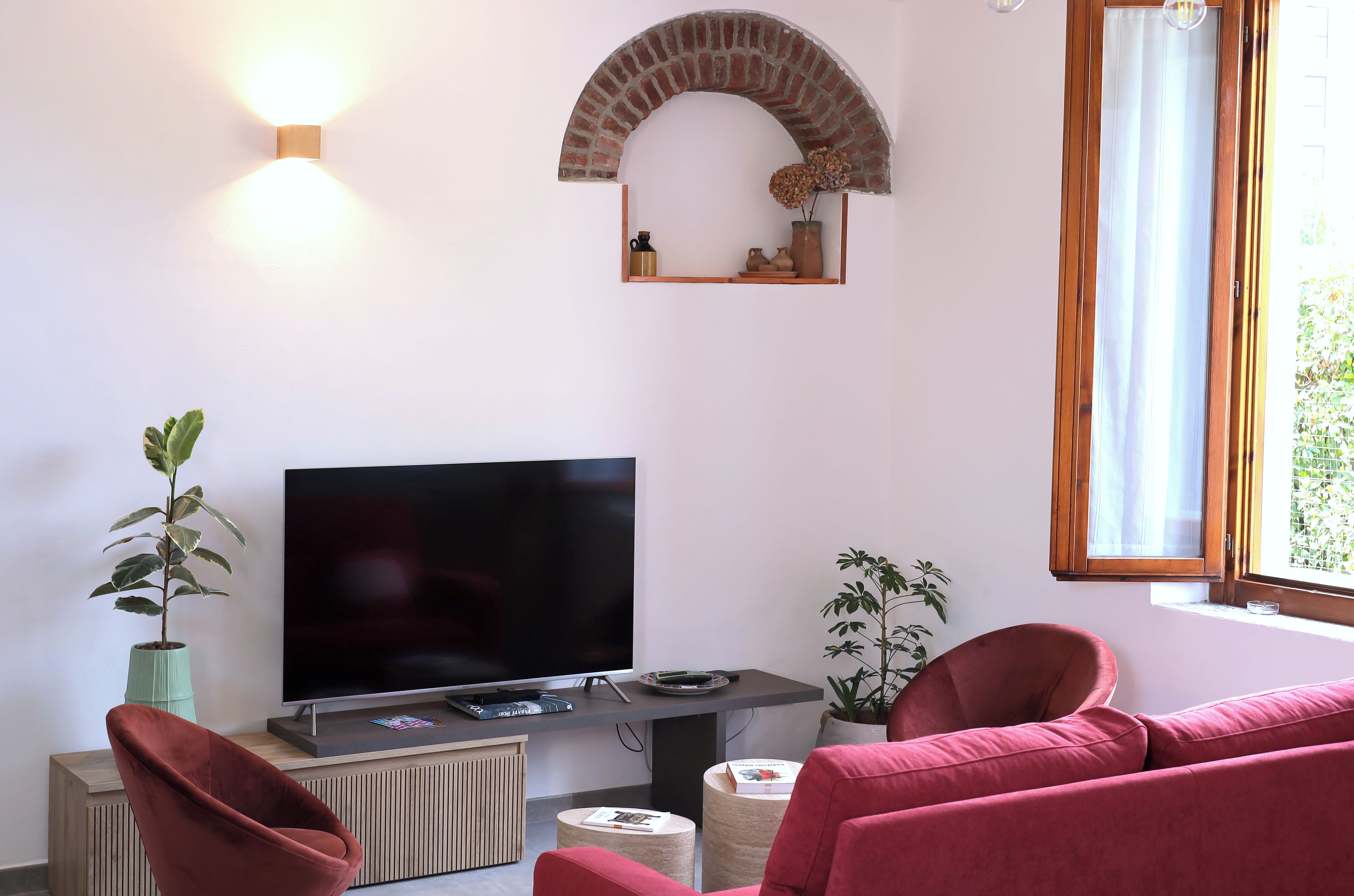 Una sala de estar con un televisor de pantalla plana, sofás rojos, una planta en maceta y un arco de ladrillo.