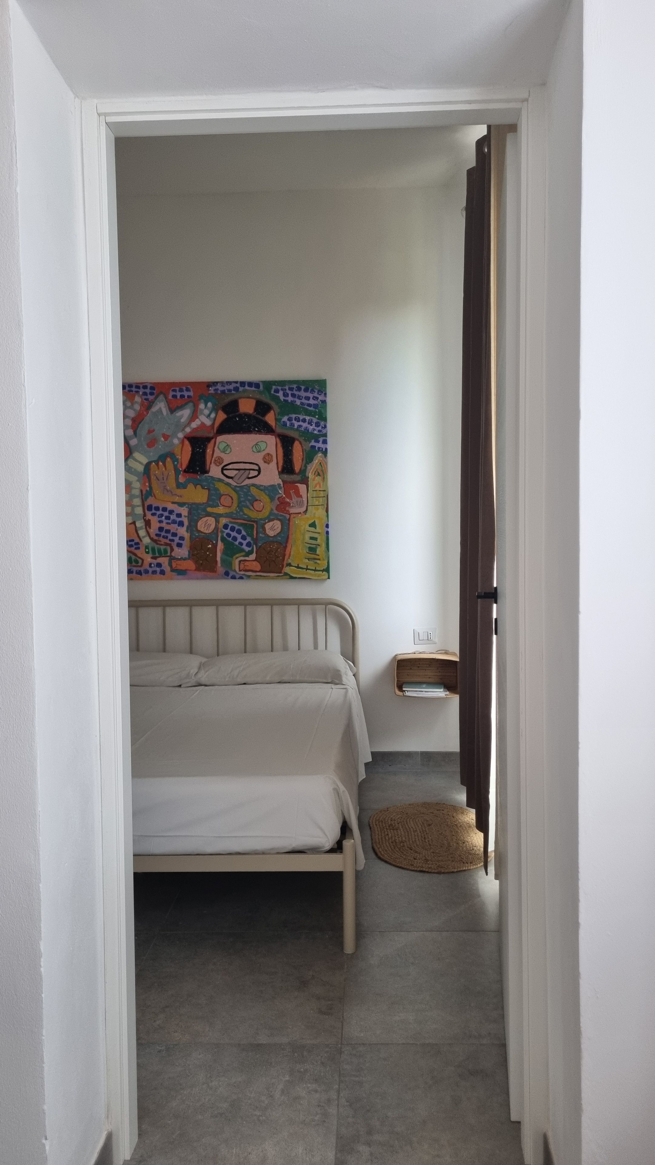 Una camera da letto con un letto, un quadro, un comodino e un tappeto.