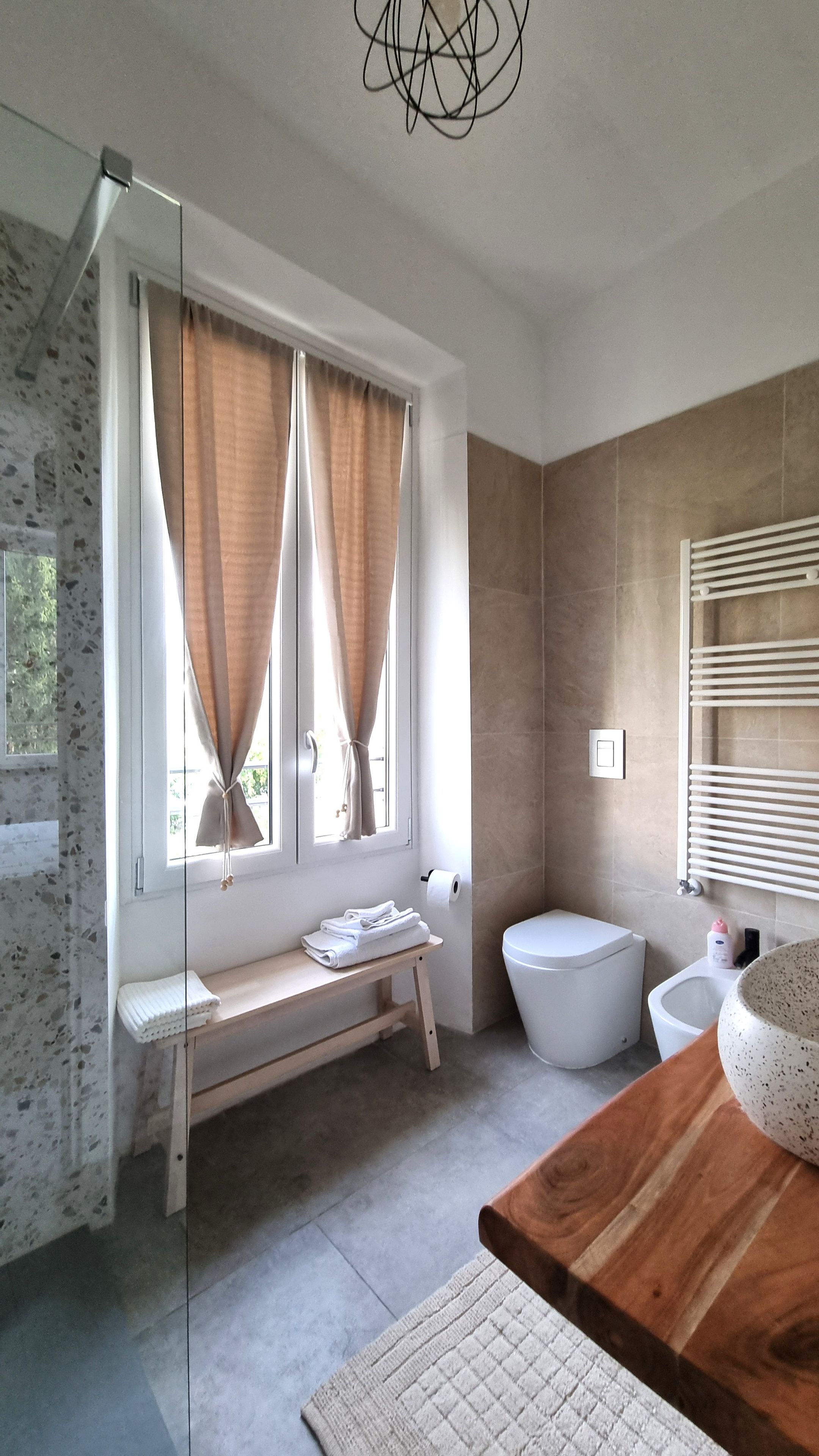 Une salle de bain moderne avec un banc en bois, des toilettes, un bidet et un grand lavabo en forme de coupe.