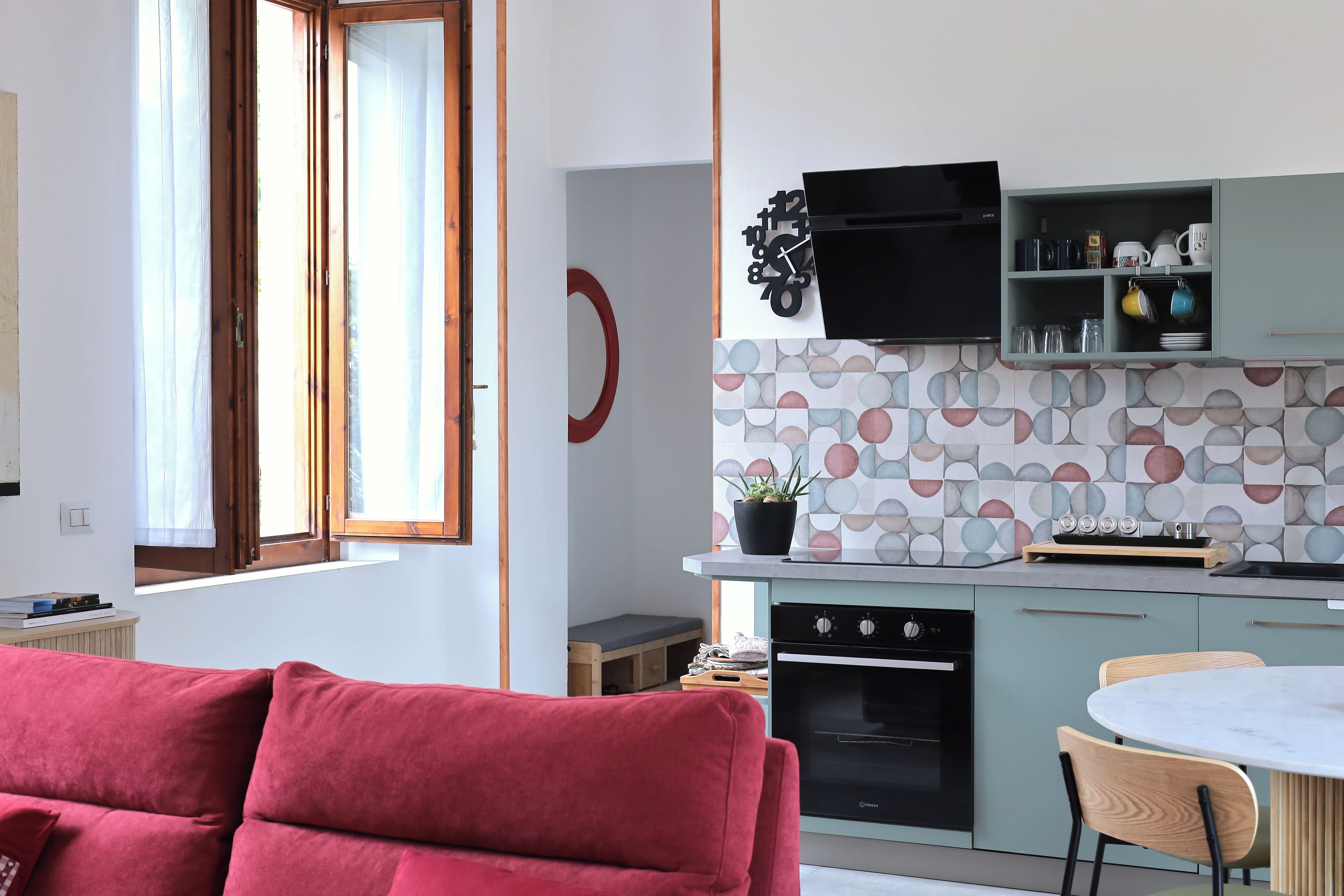 Una cocina moderna con horno empotrado, un comedor con mesa redonda y un sofá rojo en la sala de estar.