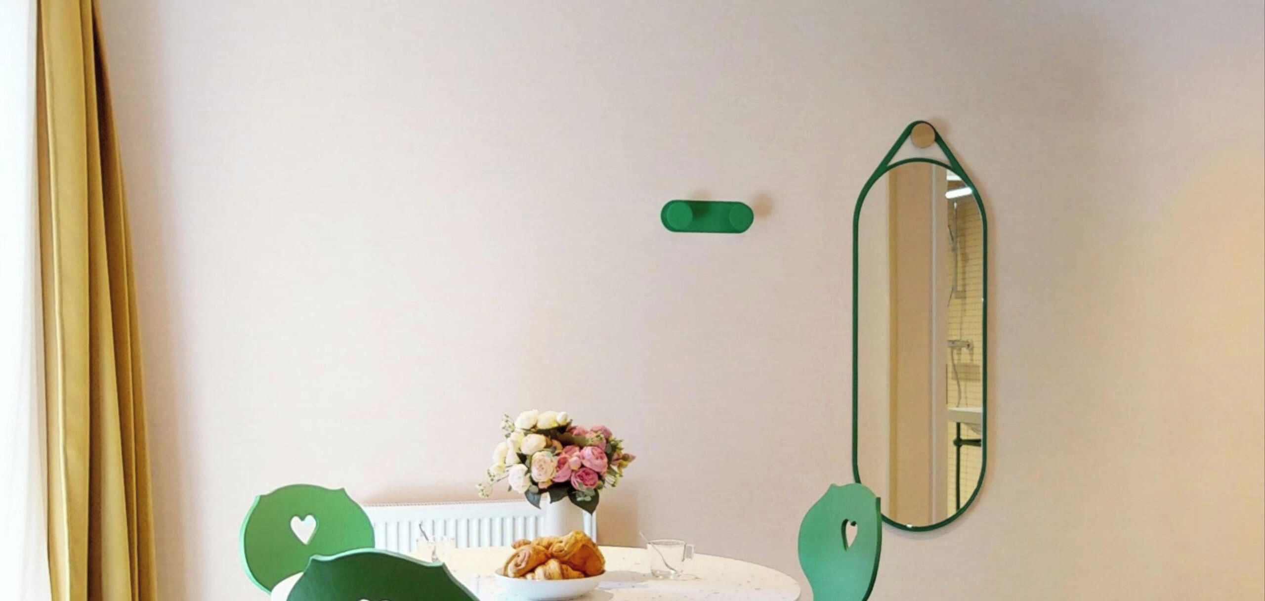 Ein Zimmer mit einem runden Tisch, einer Blumenvase, einer Platte mit Gebäck und einem Spiegel an der Wand.