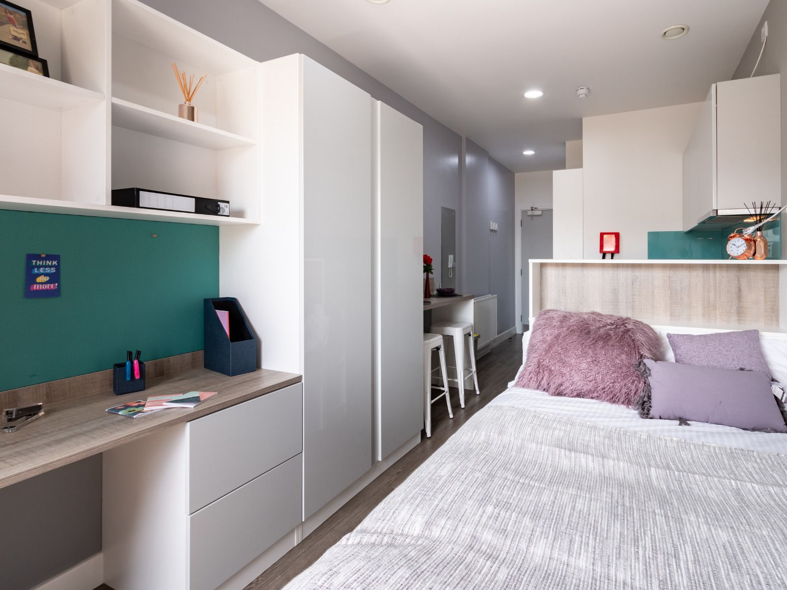 A modern bedroom with a bed, a desk, and a kitchenette.