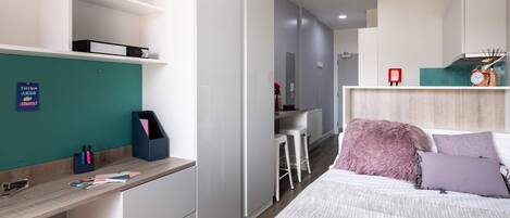 A modern bedroom with a bed, a desk, and a kitchenette.
