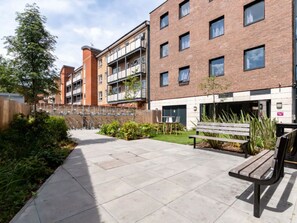 A multi-story residential building with balconies, a paved courtyard, and outdoor seating. - Student Only Kingston London (Kingston upon Thames)