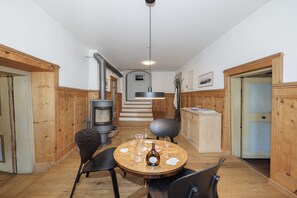 Habitació acollidora amb una taula rodona de fusta, dues cadires, una làmpada penjant i una escala de fusta que condueix a un nivell superior.