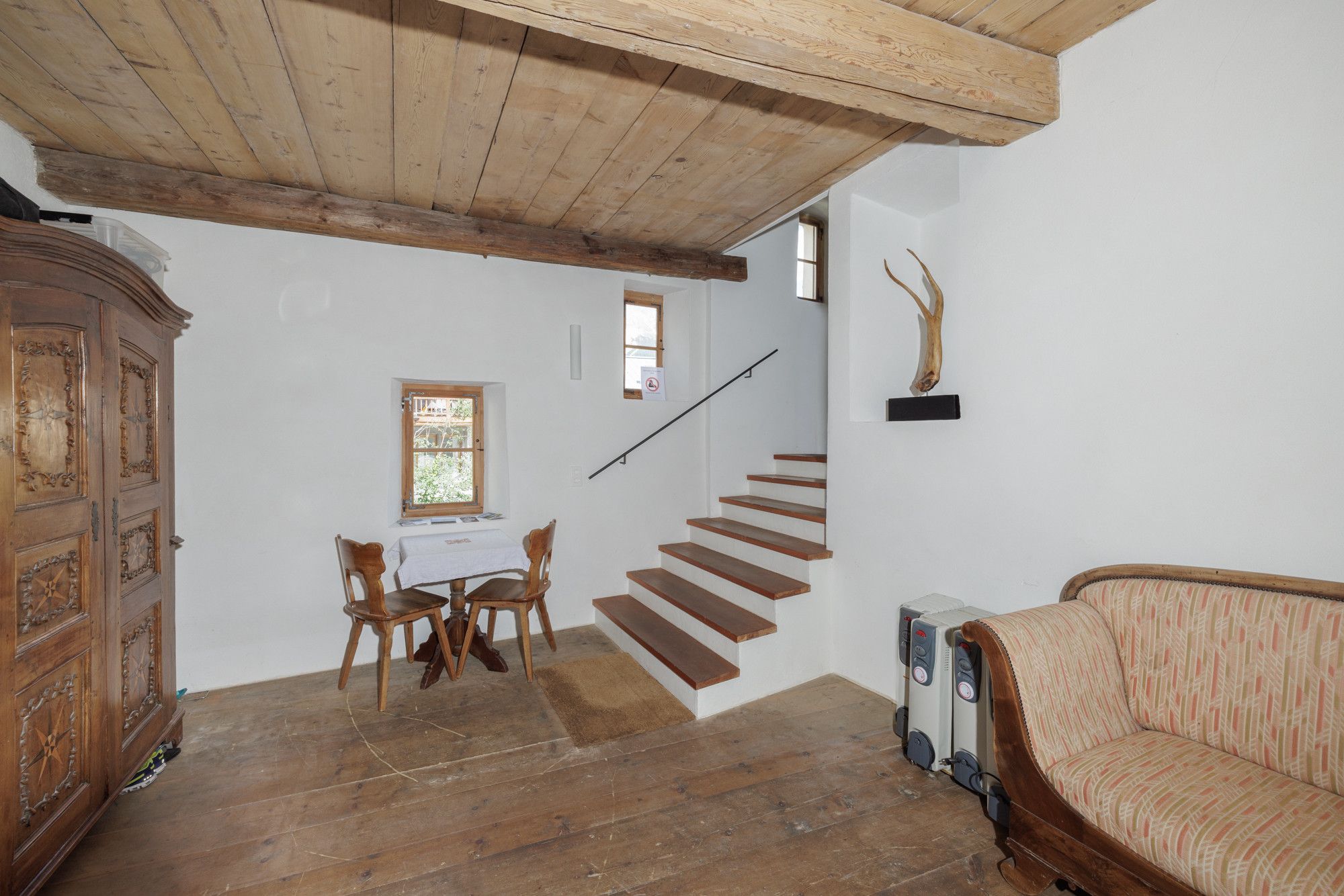 Ein Zimmer mit einer Holztreppe, einem Esstisch mit Stühlen, einem Schrank und einem Sofa.