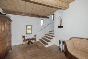 A room with a wooden staircase, a dining table with chairs, a cabinet, and a sofa. - Chasa Plaz: Cozy 4.5-room vacation rental on the village square in Sent (Sent)