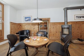 A cozy dining area with a round wooden table, black chairs, and a wood-burning stove. - Chasa Plaz: Cozy 4.5-room vacation rental on the village square in Sent (Sent)
