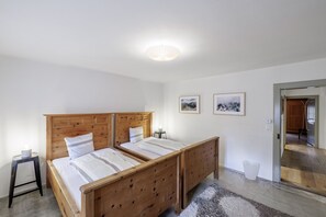 Une chambre à coucher avec un lit en bois, deux tables de chevet, un petit tabouret et deux tableaux encadrés accrochés au mur.