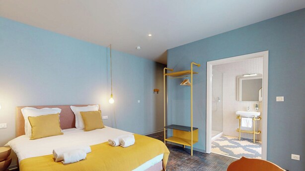 Una habitación de hotel con cama, lámparas de noche, armario y un baño visible a través de una puerta abierta.