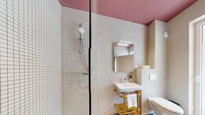 Un baño con pared revestida de azulejos formando un diseño de cuadrícula, un lavamanos blanco, un espejo y un inodoro.