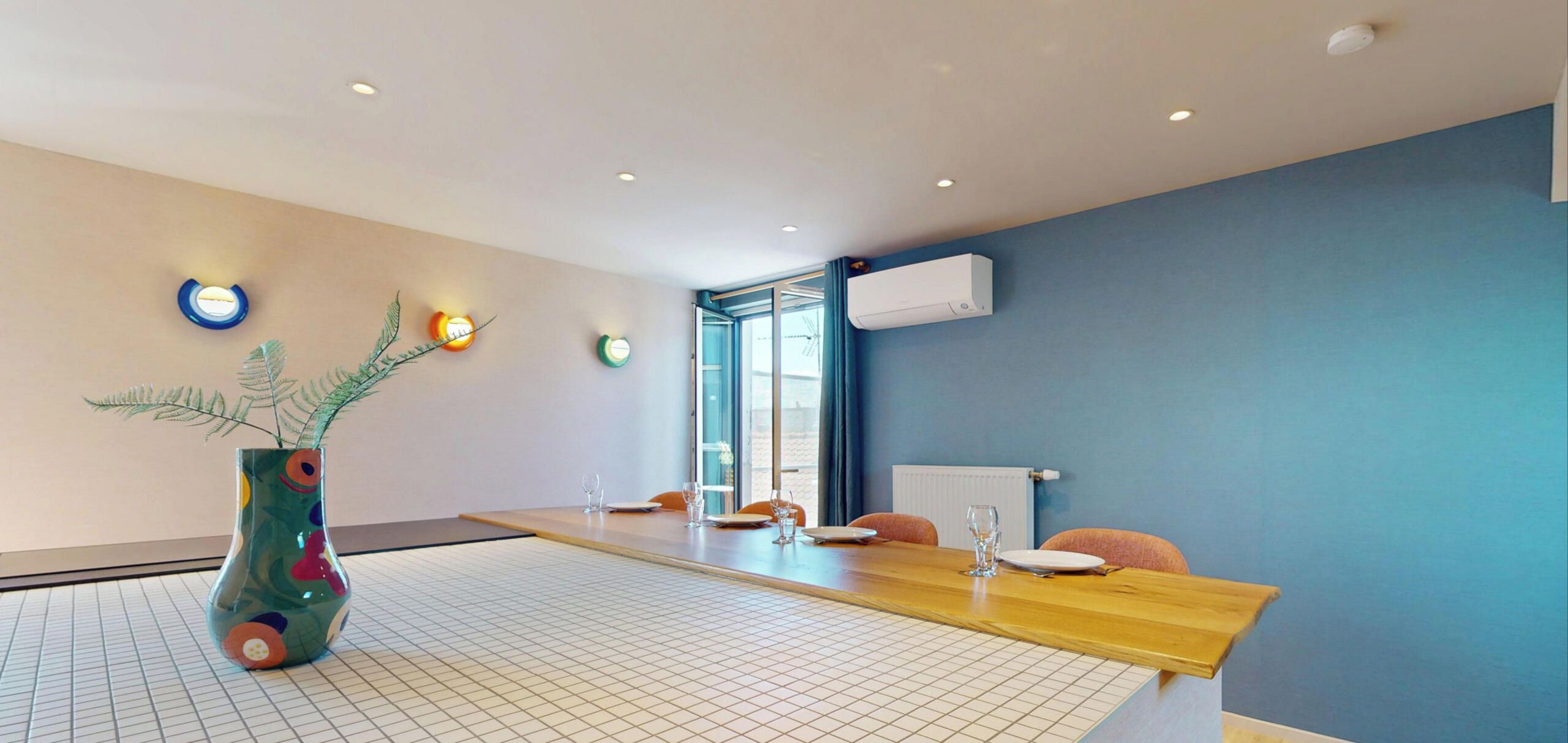 Een moderne kamer met een eettafel, stoelen, een decoratieve vaas en een raam met uitzicht.