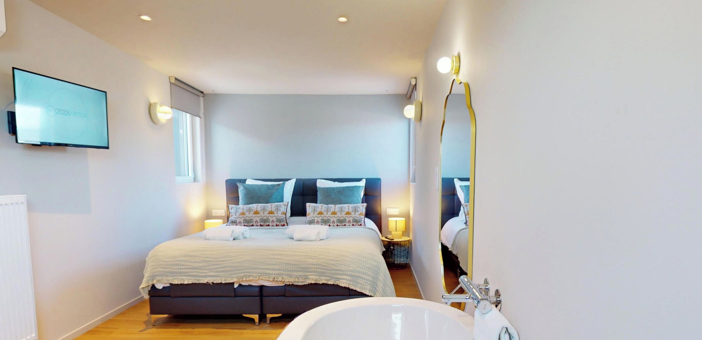 A modern bedroom with a large bed, bedside lamps, and a television on the wall.