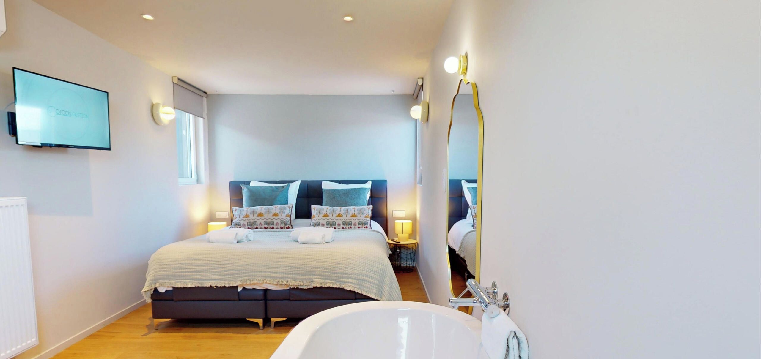 Quarto moderno com cama grande, luminárias de cabeceira e televisão na parede.
