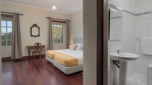 Ein Hotelzimmer mit Bett, Schreibtisch, Stuhl und einem Badezimmer mit Waschbecken und Spiegel.