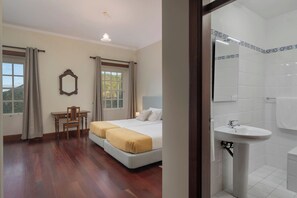 A hotel room with a bed, a desk, a chair, and a bathroom with a sink and mirror. - Vrbo Property (Santana)