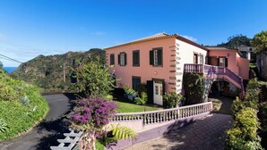 Eine pinkfarbene Villa mit einer geschwungenen Auffahrt, einer Treppe und Blick auf die umliegende Grünfläche und Hügel.