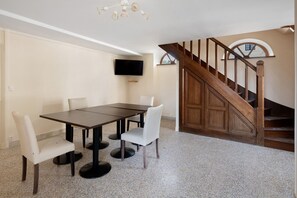 A dining area with a table and chairs, a television mounted on the wall, and a wooden staircase. - La Tour Gauche - Château Grange Arthuis (Lavau)