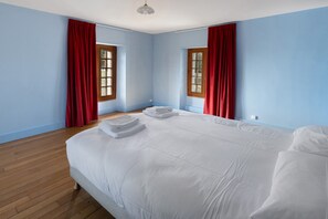 A bedroom with a large bed, two windows with curtains, wooden flooring, and a ceiling light. - La Tour Gauche - Château Grange Arthuis (Lavau)
