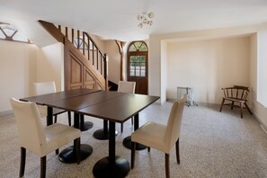 A dining area with a wooden table and four chairs, a staircase, and a radiator. - La Tour Gauche - Château Grange Arthuis (Lavau)