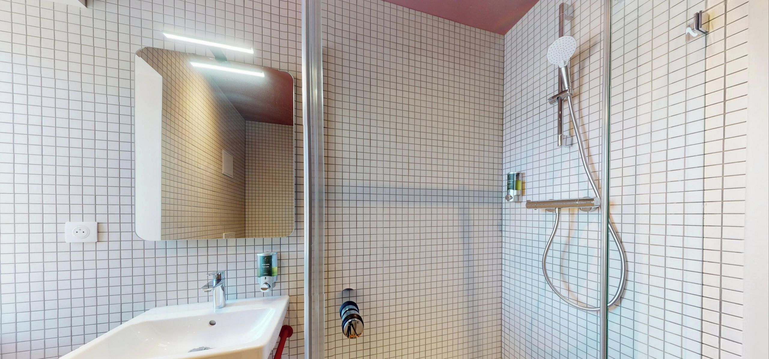 Ein Badezimmer mit einem weißen Waschbecken, einem Spiegel und einer Dusche inklusive Handbrause.