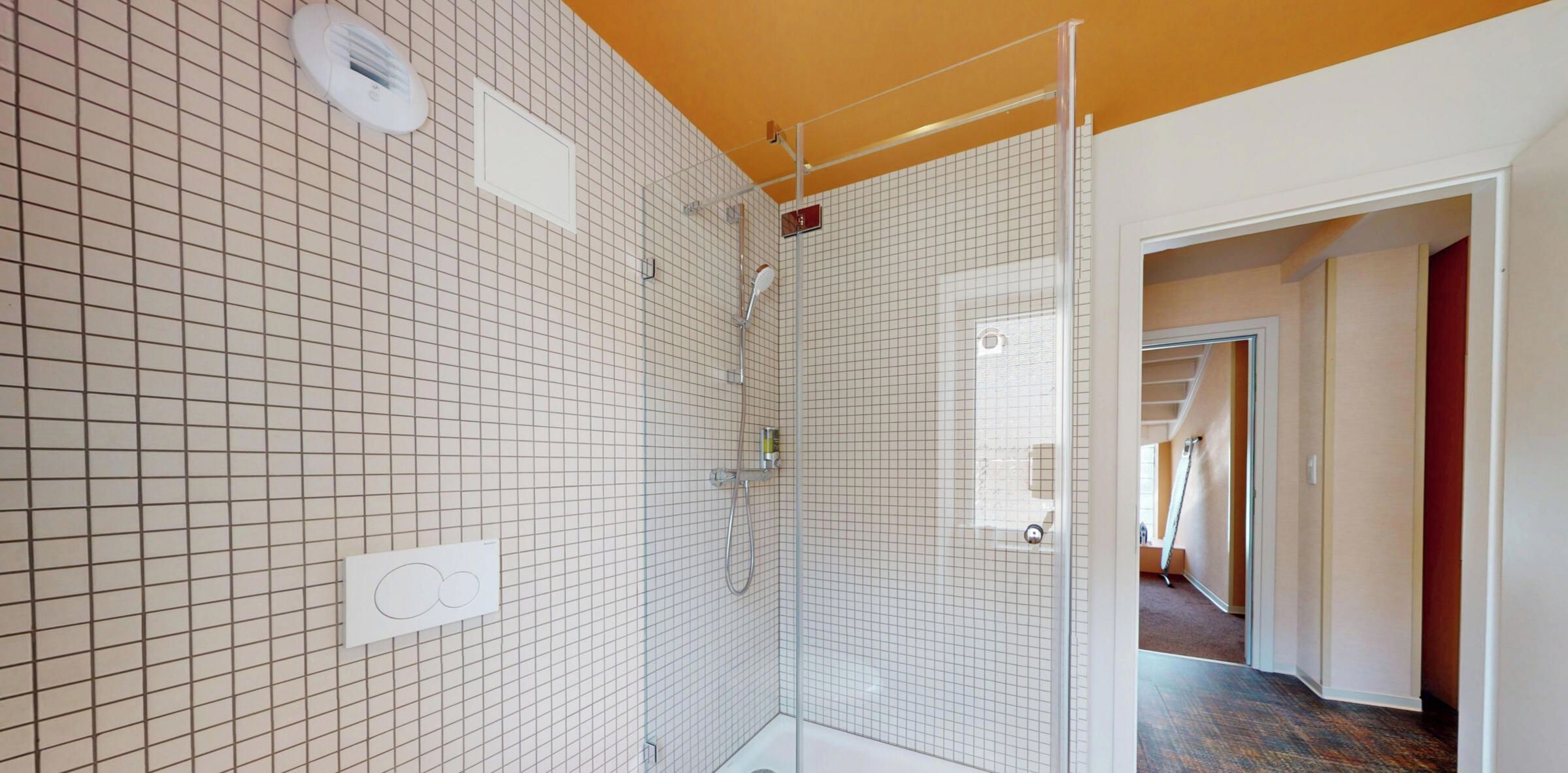 Ein Badezimmer mit Dusche, geflieste Wände und einer sichtbaren Tür zu einem anderen Raum.