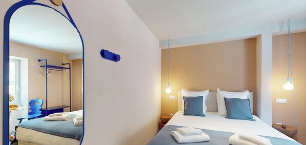 Una habitación de hotel con cama, mesita de noche, lámpara y espejo.
