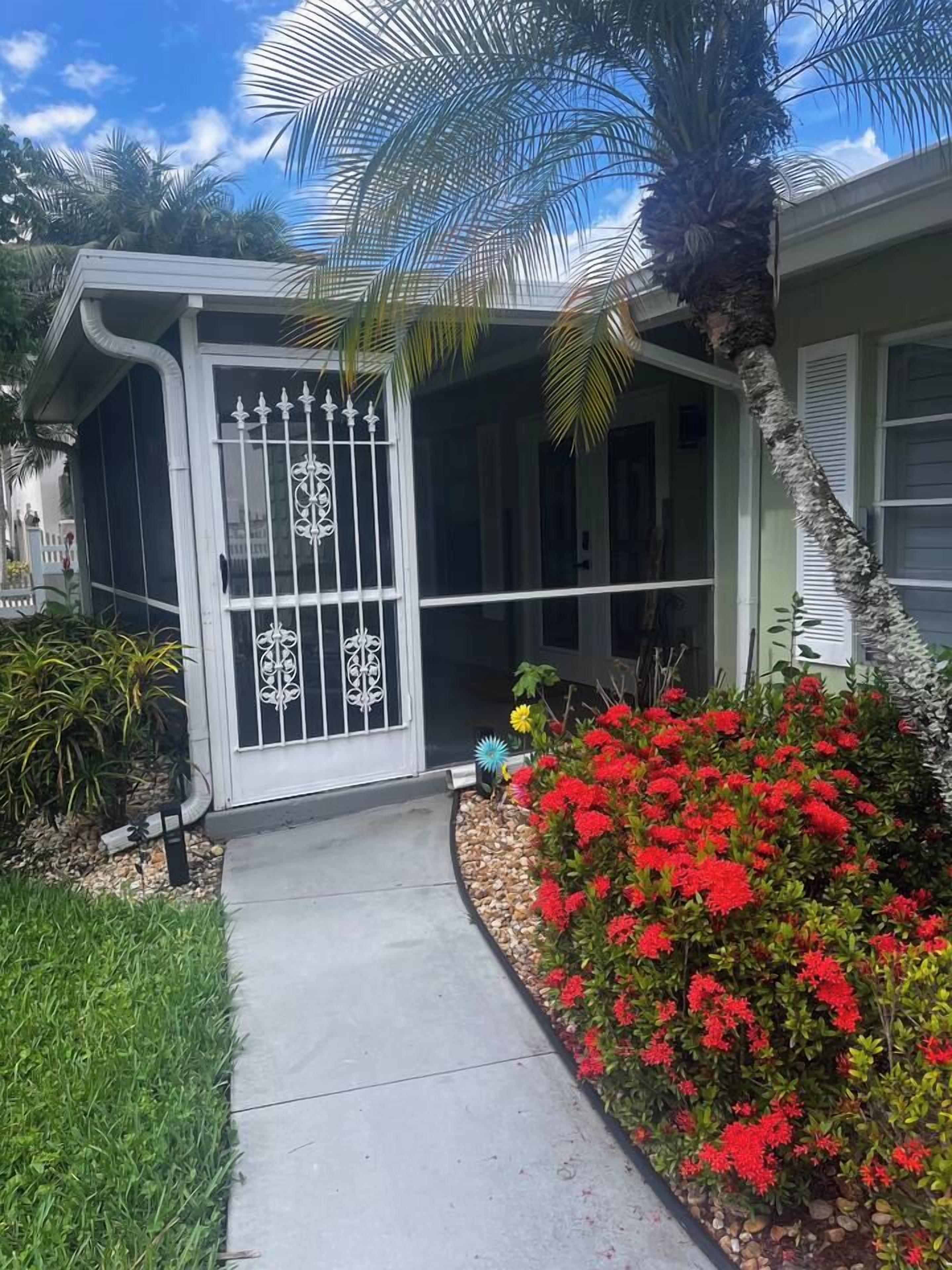 A house with a gated entrance, a covered porch, and a garden with red flowers.