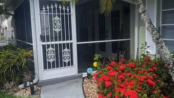 A house with a gated entrance, a covered porch, and a garden with red flowers.