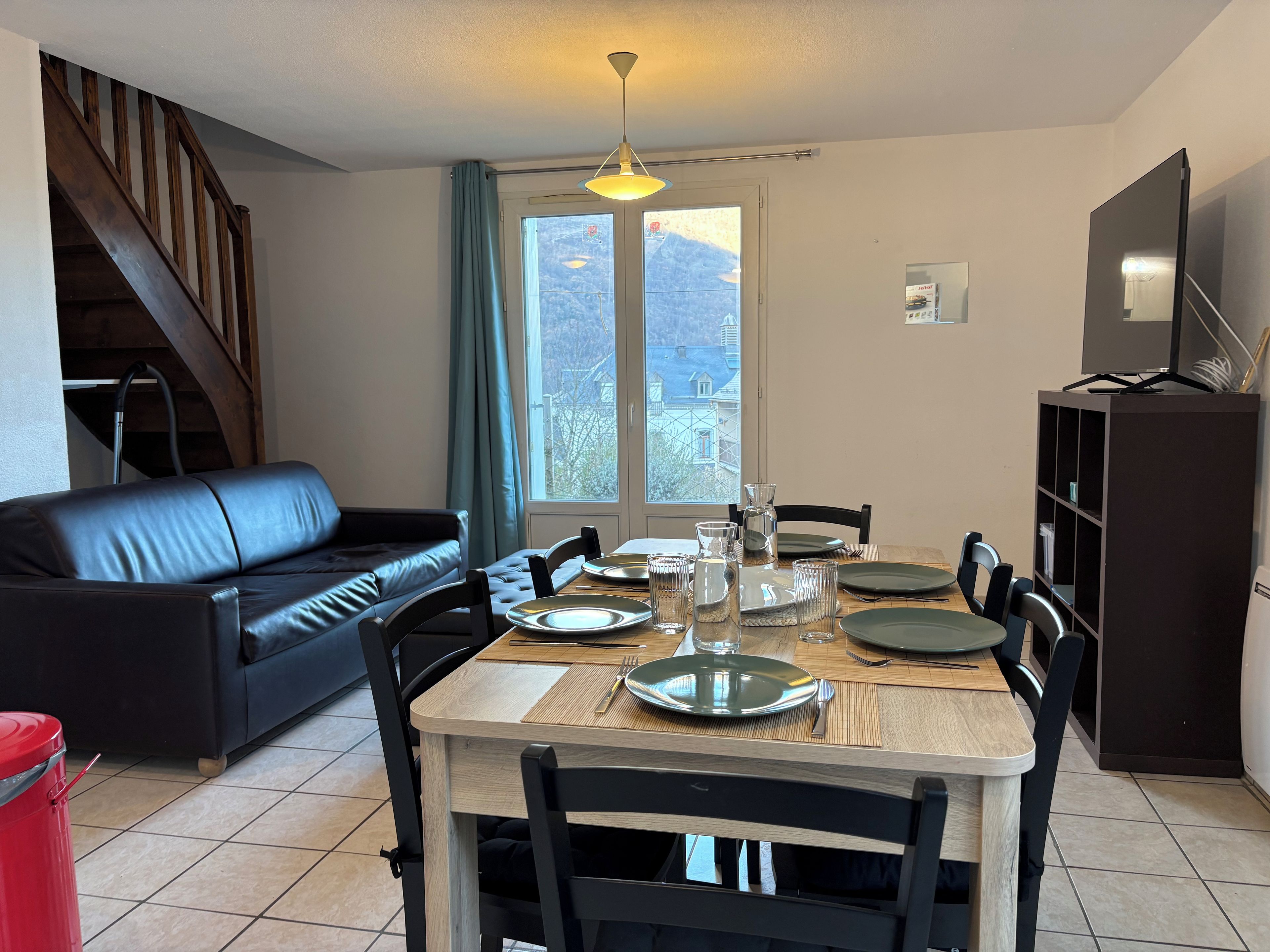A dining area with a table set for four, a sofa, a TV, and a staircase.
