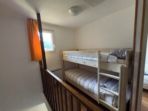 En køjeseng med et vindue over og et trægelænder, samt en lampe i loftet.