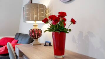 A wooden table with a red vase of flowers, a lamp with a grid-patterned lampshade, and a small card stand with a brochure.